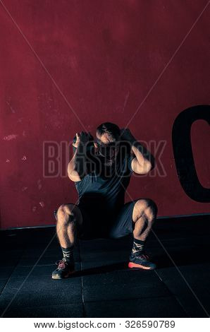 Young Bearded Atletic Man Holding Dumbbell  And Doing Squats In The Modern Gym. Man During Workout G