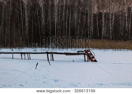 Old Wooden Pier In The Snow. Dense Forest In The Background. Frosty Morning