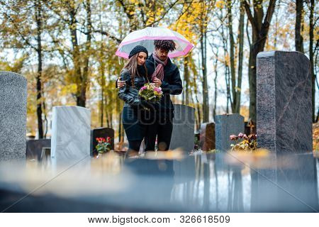 Couple mourning a deceased loved one on cemetery in fall standing between the graves