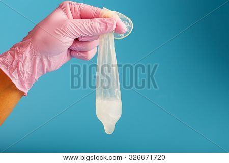 Latex Condom Contraception With Sperm, A Doctor In A Pink Glove Holds A Full Used Condom On A Blue B