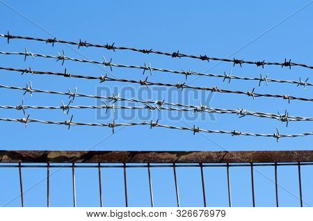 Close-up Of A Barbed Wire Fence In Front Of The Clear Bright Blue Sky