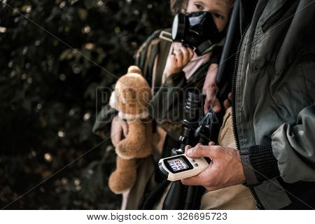 Cropped View Of Man Holding Radiometer Near Kid In Gas Mask, Post Apocalyptic Concept