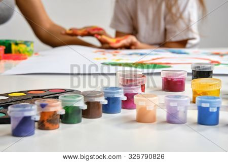 Little Artist In White T-shirt Standing At Table With Whatman And Colorful Paints, Painting On It Wi