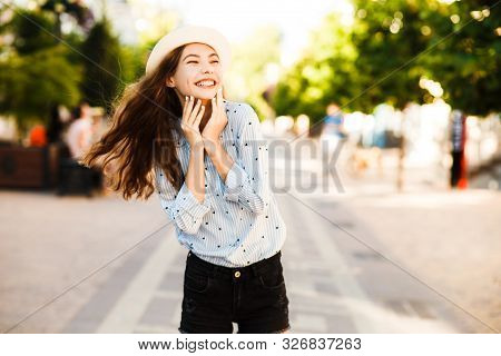 Emotional Girl Teenager In A Hat Walks Through The Summer City. Debonair Caucasian Girl Enjoying Pho