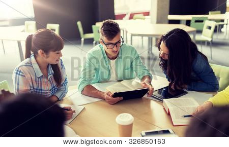 education, high school, people and technology concept - group of international students sitting at table with tablet pc computers, books and notebooks at university
