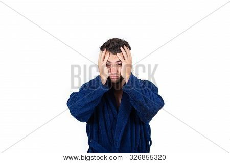 Portrait Of Tardy Young Man Wears Blue Bathrobe Holding Hands To Head, Unable To Wake Up In Time To 
