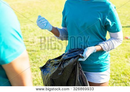 Eco Volunteer Collecting Trash Outside. Young Woman Wearing Uniform And Protective Gloves, Holding P