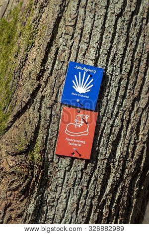 Freudenberg, Germany - Apr 6, 2018: Sign At A Tree Shows The Direction Of St. James Way And The Taub
