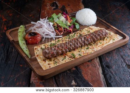 Turkish lula lamb or beef kebab with rice and vegetables isolated on rustic wooden table 