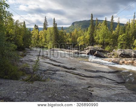 Beautiful Northern Landscape With Wild Glacier River Kamajokk, Boulders And Spruce Tree Forest In Kv