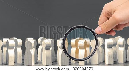 A Magnifying Glass Looks At A Crowd Of Wooden Figures Of People. Society, Demographic. Group Of Citi