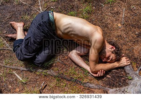 A Young Shamanic Topless Guy Lies Down Close To Nature, Embracing Tree Roots During Relaxation And M