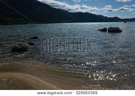 Late Afternoon Sunlight Stricks The Boulders And Sandy Beach In Lake Tahoe