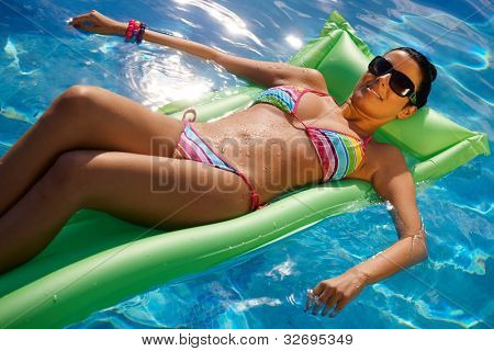 Sexy giovane donna posa sul materassino in bikini nel centro della piscina.