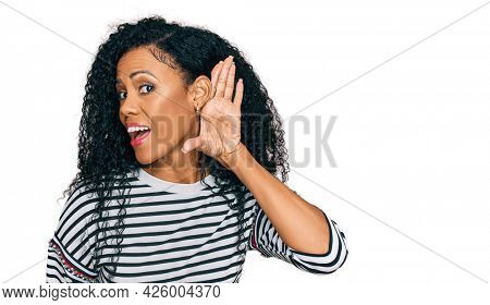 Middle age african american woman wearing casual clothes smiling with hand over ear listening an hearing to rumor or gossip. deafness concept. 