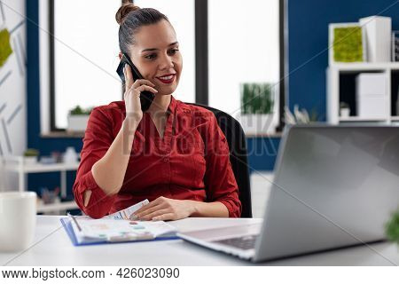 Smiling Entrepreneur Having A Conversation During Phone Call With Colleagues, Checking Finance Chart