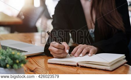 Close Up Hand Of Woman Hand Holding Pen Taking Note And Working With Laptop At The Table Office