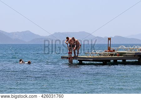 Hisaronu, Turkey​ -​ July 2021: Two Men Lower A Joyful Girl In A Bikini Into The Sea Holding Her Han