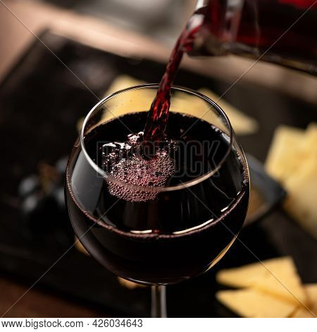 Expensive Red Wine Pouring Into Wine Glass. Wineglass With Merlot Or Sauvignon On Blurred Background