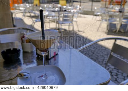 Ice Coffee, Cafe Shakerato In Glass Close-up On The Table Across Restaurant Furniture And City View.