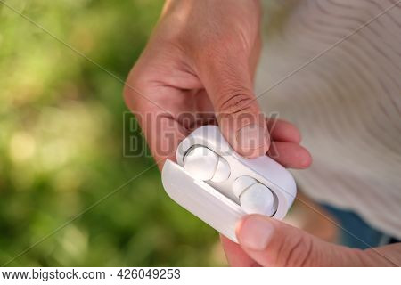 Woman Hand Open A Case With Wireless Headphones, Outdoors, In The Blurry Background.