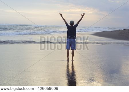 Man Standing Alone On The Beach, With Arm Raised Against The Sea At Sunset. Freedom And Self Healing