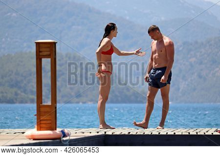 Hisaronu, Turkey - July 2021: Young Couple Is Arguing Standing On A Beach On Mountains Background. S