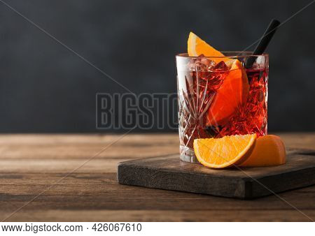 Negroni Cocktail In Crystal Glass With Orange Slice And Black Straw On Chopping Board On Wood Backgr