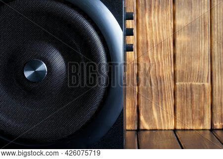 A Large Loud Subwoofer In A Wooden Case With A Metal Grille And Volume And Tone Controls Stands Agai