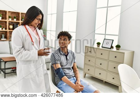 Young latin doctor woman smiling happy measuring pulse using tensiometer at the clinic.