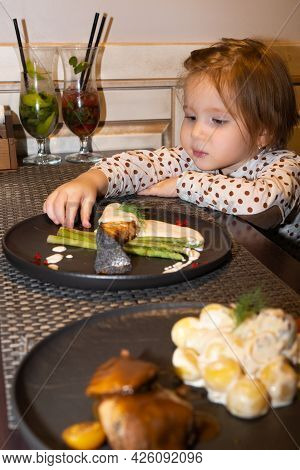 A Little Girl In A Restaurant Looks At A Freshly Brought Fish Dish On The Table In Front Of Her And 