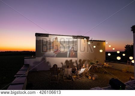 Small Group Of People Watching Movie On The Rooftop Terrace At Sunset. Open Air Cinema Concept. Roma