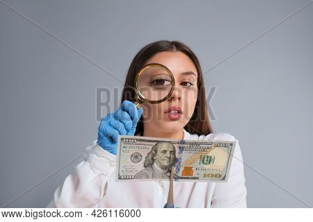 Expert Authenticating 100 Dollar Banknote With Magnifying Glass On Light Grey Background. Fake Money