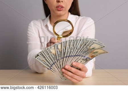 Expert Authenticating 100 Dollar Banknotes With Magnifying Glass At Table On Light Grey Background, 