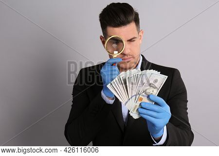Expert Authenticating 100 Dollar Banknotes With Magnifying Glass On Light Grey Background. Fake Mone