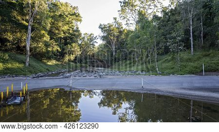 A Country Creek With Water Reflections On One Side Of The Road And A Fishway On The Other. Palm Tree