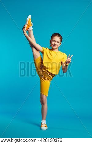 Flexible Adorable Cute Child Girl In Yellow Sportswear Perform Transverse Twine And Showing Peace Ge