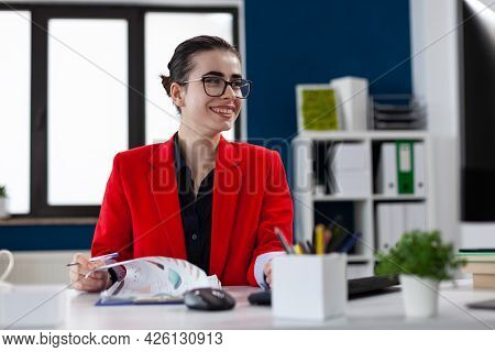 Smiling Cheerful Businesswoman Doing Paperwwork In Corporate Office, Workplace , Looking At Computer