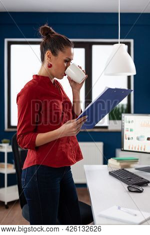 Successful Business Woman In Company Office Looking Through Charts While Holding And Ejoying A Cup O