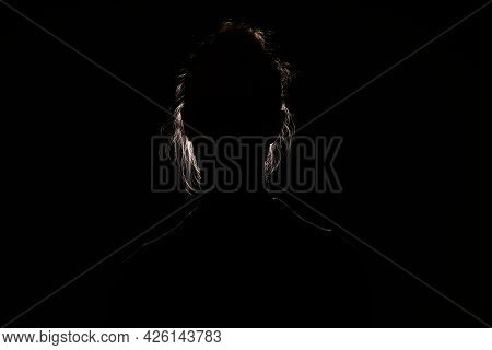 Backlit Portrait Silhouette Of Unrecognizable Woman Hiding Face And Identy In The Dark Shadow