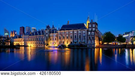 View of the Binnenhof House of Parliament and the Hofvijver lake with downtown skyscrapers in background illuminated in the evening. The Hague, Netherlands