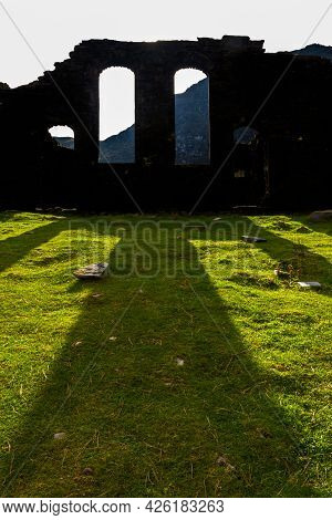 Spectacular Sun Behind Silhouetted Ruined Gothic Church, Throwing Light Onto Green Grass.