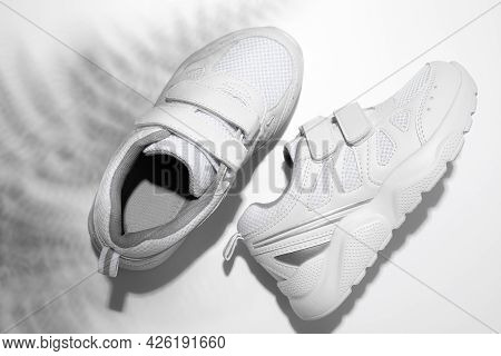 Top View Two White Sneakers With Hard Summer Sunny Fern Shadows On A White Background