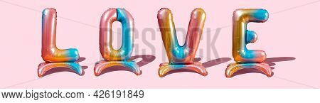 some multicolored letter-shaped balloons forming the word love on a pink background,  in a panoramic format to use as web banner or header