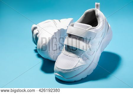 Close-up Of Two White Girly Sneakers With Velcro Fasteners Isolated On A Blue Background, One Sneake