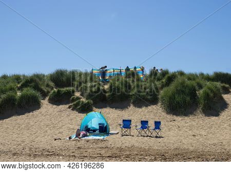 Old Hunstanton, Norfolk, England - June 13 2021. Woman Lying On A Towel Near A Blue Tent With Three 