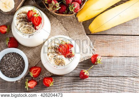 Dessert With Yogurt, Strawberries, Banana, Chia Seeds, Served In Glass Jars On A Wooden Table, Delic