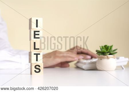 Pyramid Of Wooden Cubes With The Word Ielts In The Foreground, In The Background - Business Woman Wo