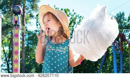 Cute Little Girl Eating A Huge Piece Of Cotton Candy In An Amusement Park On A Summer Day. Happy Chi