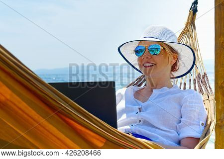 Work From Anywhere. Young Smilyng Woman, Female Freelancer In Straw Hat Working On Laptop On Beach.